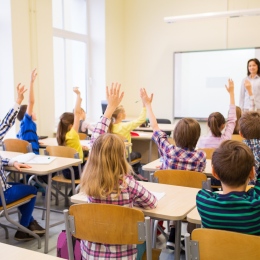 Grupp av elever i klassrum som räcker upp händerna.