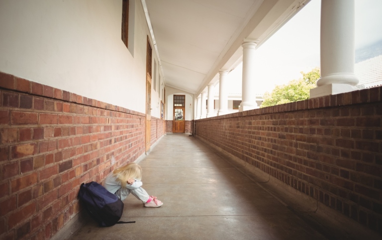 Sad child sitting alone on the floor in a corridor.
